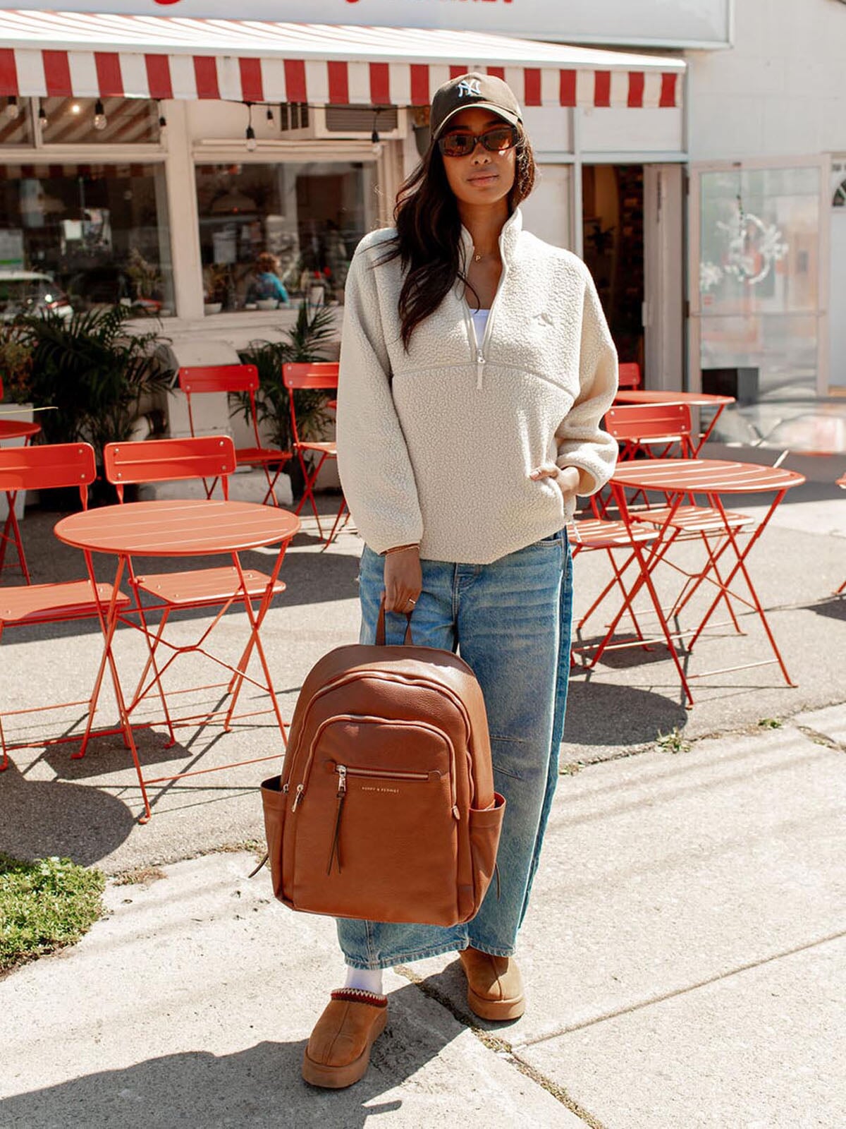 Woman holding a brown vegan leather backpack in an outdoor cafe setting